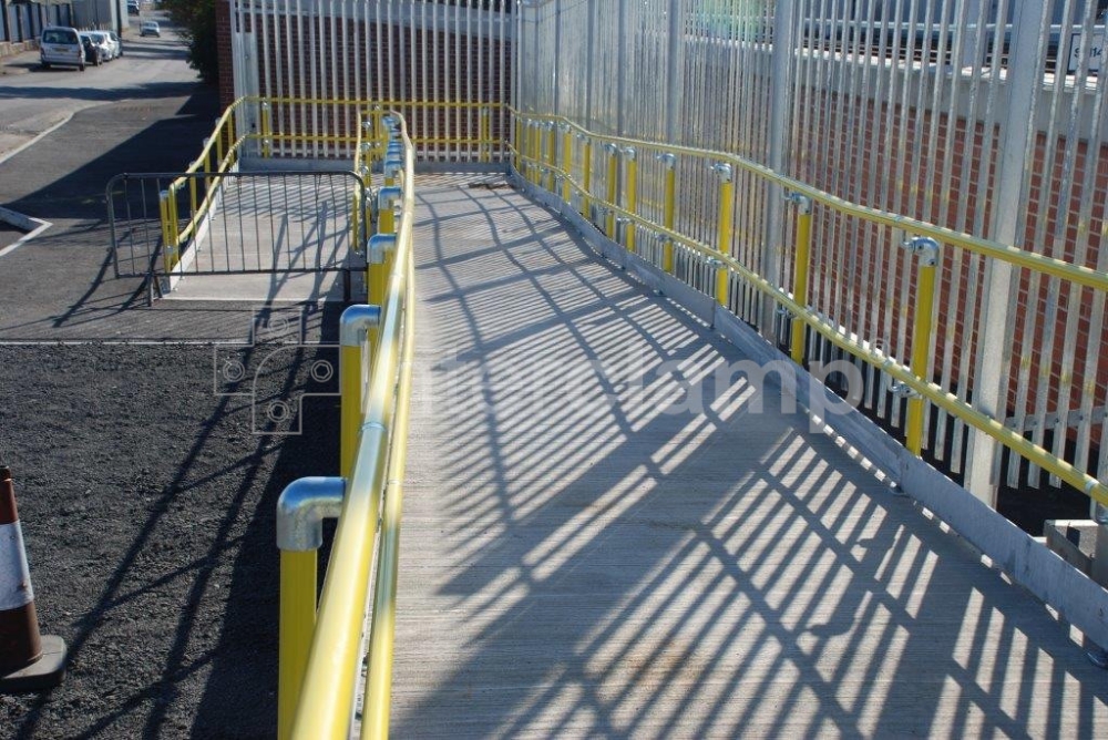 Safety yellow powder-coated handrail tube and Interclamp Key Clamp DDA Assist fittings used to ensure a reliable and accessible disabled access ramp at a train station.